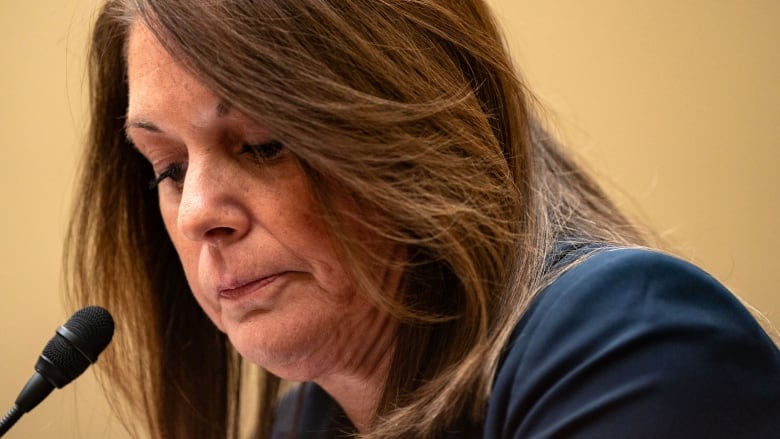 A woman in a navy blue suit looks down as she appears at a hearing.