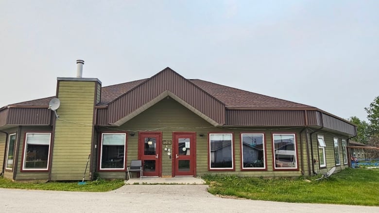 The outside of a light-coloured building with reddish doors is seen in the summer.