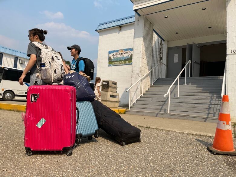 People pulling luggage outside a community hall.