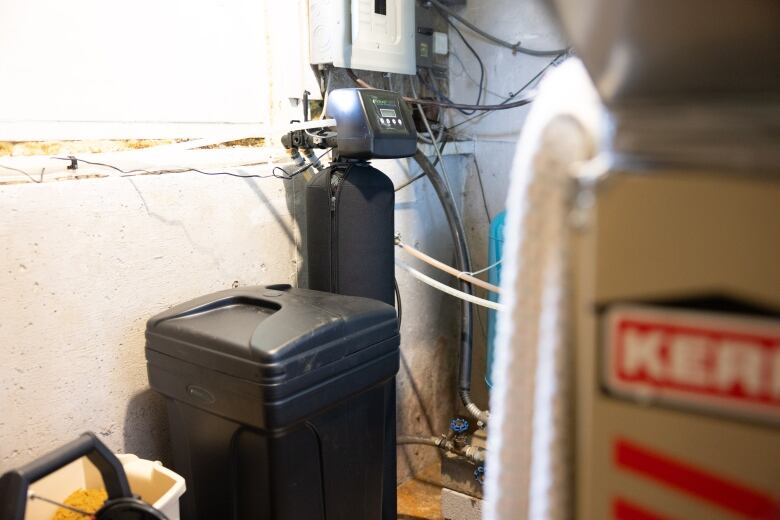 A water softener system consisting of a square black plastic bin and a cylindrical black tank with a digital meter on top. 