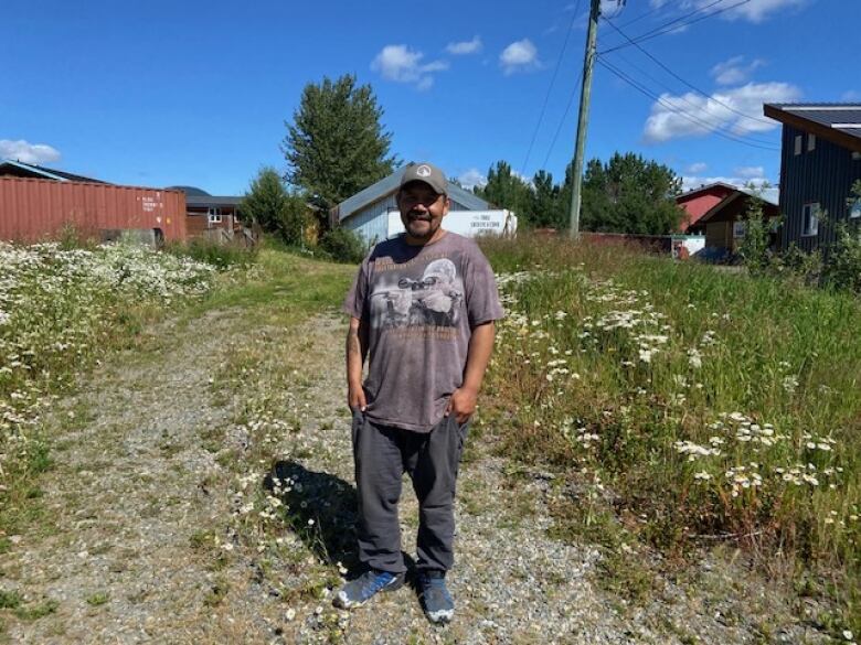 A man stands in a gravel field of weeds with old small houses behind him