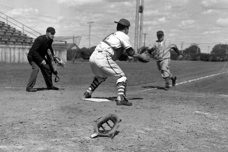 An umpire watches as a baserunner charges to home plate while a catcher catches a ball in his glove.