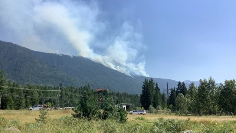 Smoke rises from the mountains, with some trailers in the foreground.