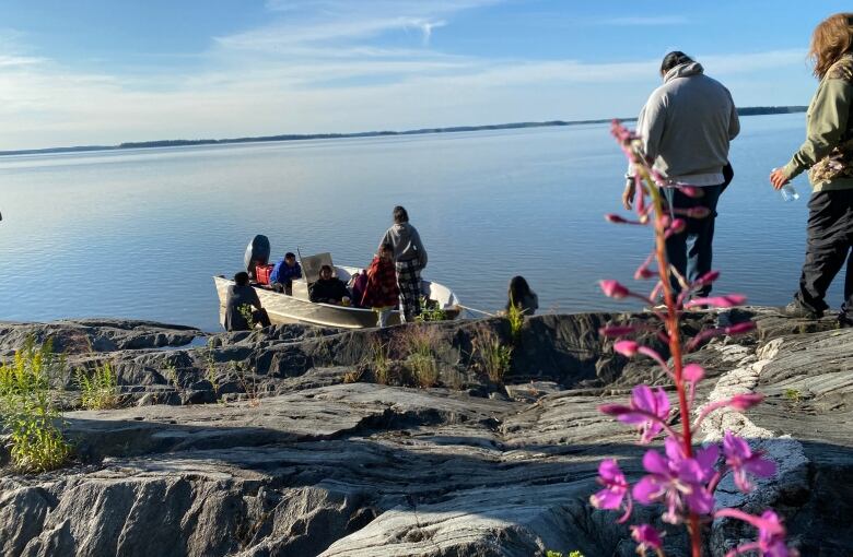 People stand on rocks with a boat on shore and a lake in the background.