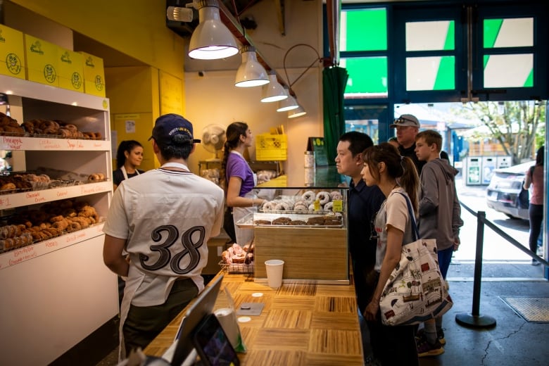 Patrons stand behind the counter of a donut shop in a market. 