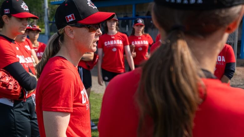 A woman in a red shirt talks to a group of women baseball players.