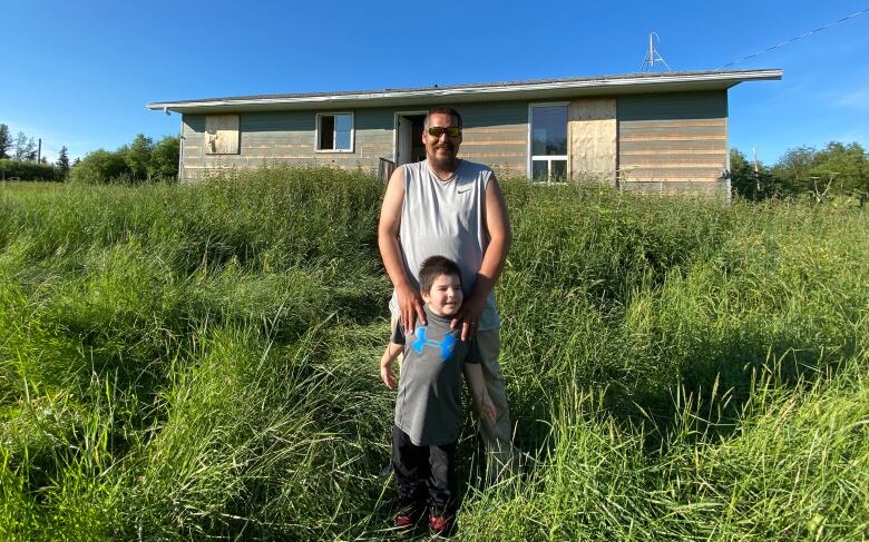 A man stands with his kids outside a home with really grass.