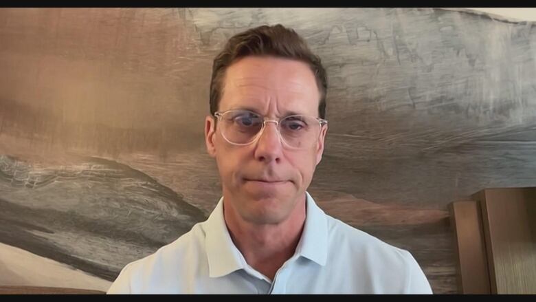 A man in a white button up shirt with glasses against a wooden background.