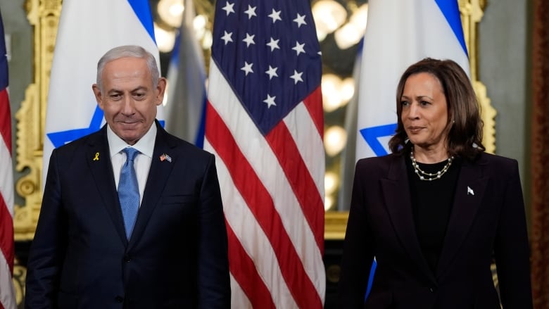 A woman and a man wearing suits stand in front of Israeli and U.S. flags. 