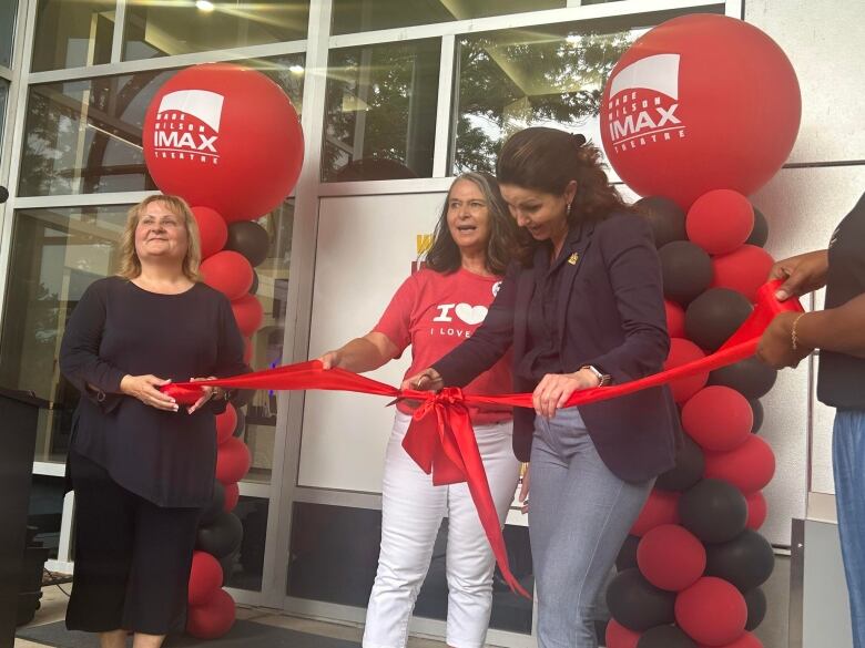 Three women at a ribbbon cutting. 