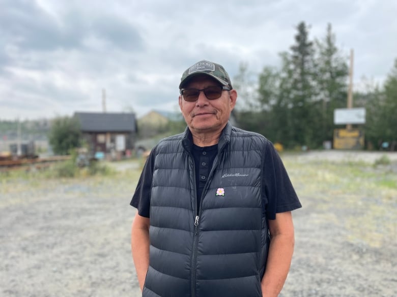 A man wearing a black t-shirt and puffy vest with a ballcap on.