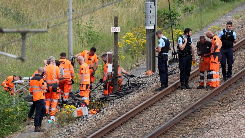 Several workers on reflective bright uniforms and police officers in uniform are shown standing on train tracks.