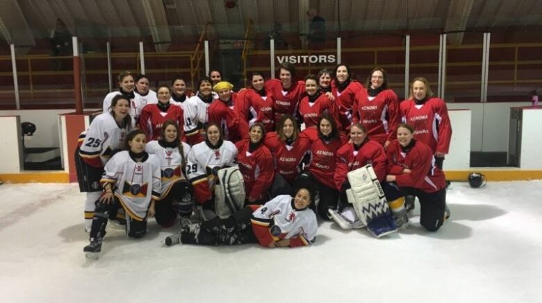 A group of hockey players pose for a team photo on the ice of an indoor rink.