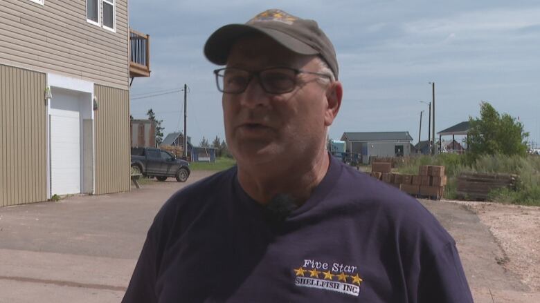 Man in a navy T-shirt and ballcap labelled Five Star Shellfish Inc. stands outside near an industrial building.