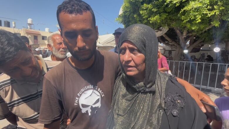 A man in a brown shirt has his arm around a woman in a black dress and green headscarf