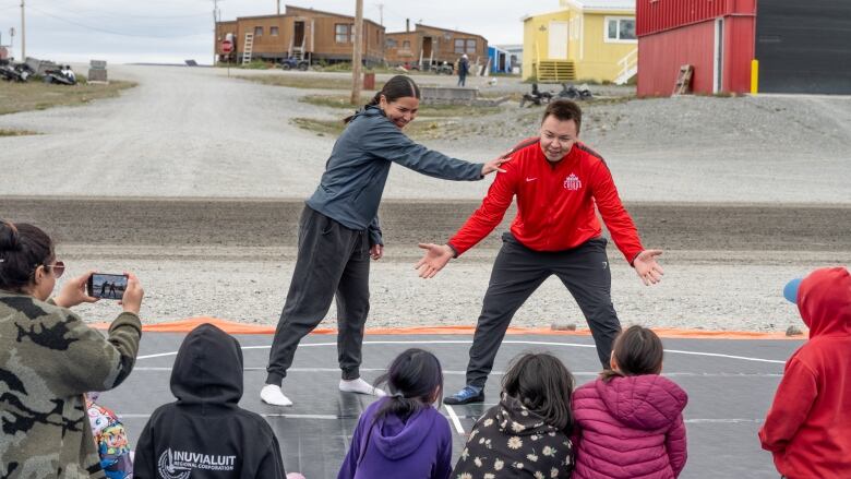 a man an a woman wrestle on a black mat as kids look on 