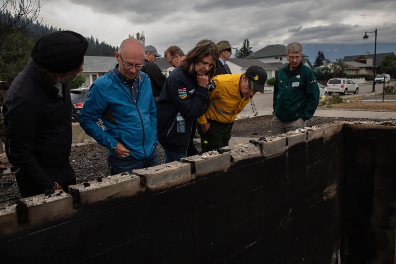 Jasper Mayor Richard Ireland, second from left, looks at the remainder of his home in Jasper, Alta., on Friday, alongside federal Emergency Preparedness Minister Harjit Sajjan (first from left), Alberta Premier Danielle Smith (third from left) and others reviewing the damage.