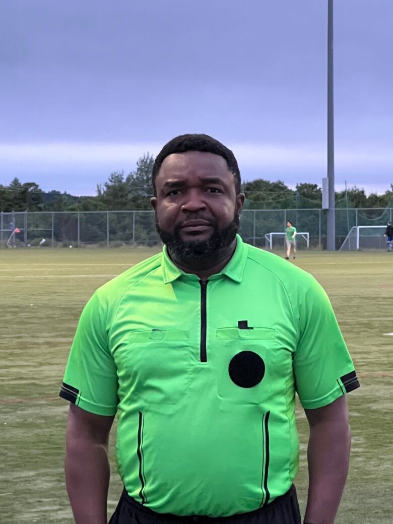 Black man with beard wears a neon green referee t-shirt and stands on a soccer field