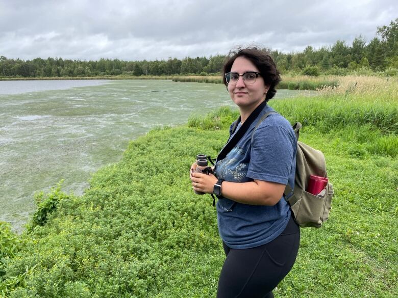 A young person holding binoculars while standing next to a lake.