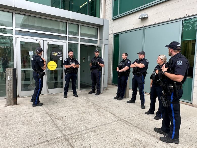 Seven police officers stand near a glass door.