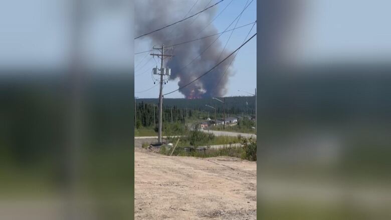 Smoke plume billows behind a mountain with trees