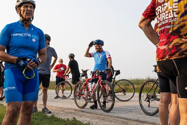 A group of people wearing cycling gear are standing holding bikes on a rural road.