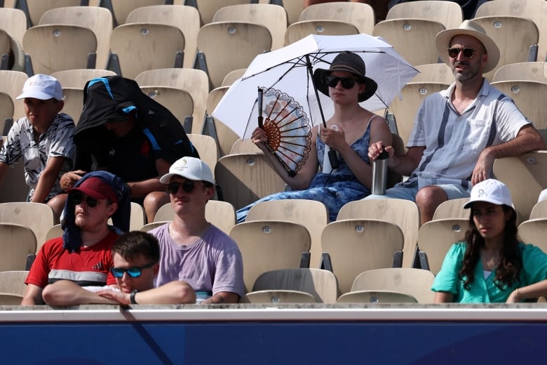 People sit in stadium seats with  fans and umbrellas