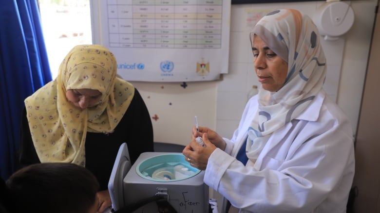 a woman in hijab and a white doctor's coat prepares a shot for a child 