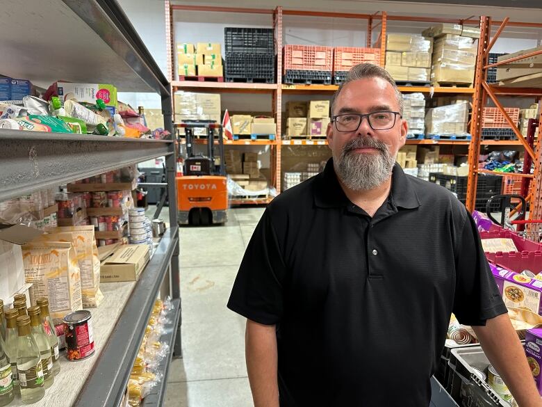 A man stands beside shelves of food.