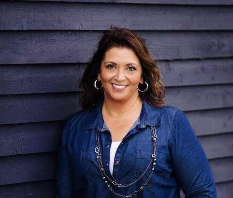 A woman in a jean shirt smiles as she leans against a striped wall.