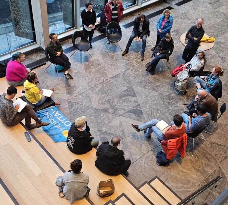 A group of people sit in a circle in a public space with good natural light.