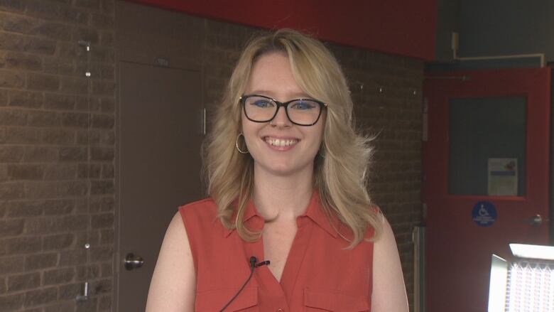 Woman with blonde hair in an orange shirt smiles.