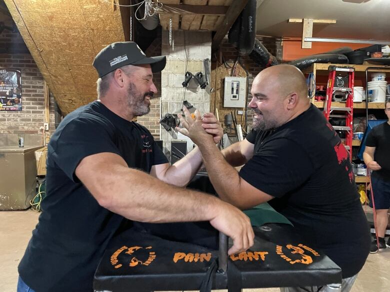 Two men in black shirts lock hands and prepare to arm wrestle. 