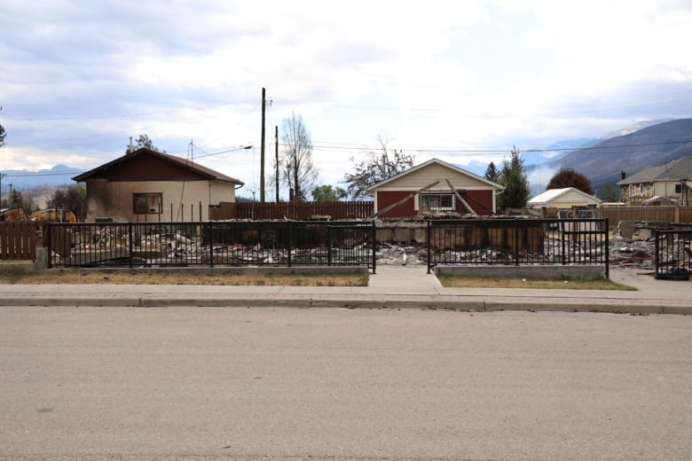 Houses behind a black fence with black soot and debris on the ground. 