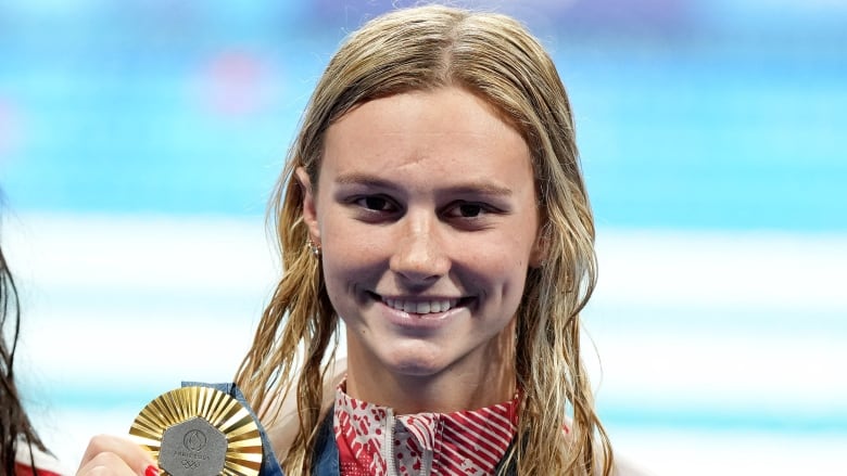 A female athlete smiles as she poses with a gold medal around her neck.