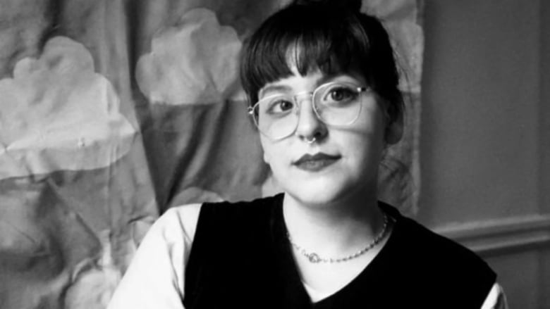  A black and white image of a white woman with her hair in a bun, wearing glasses. 