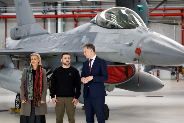 Ukrainian President Volodymyr Zelenskyy is flanked by Belgian Prime Minister Alexander De Croo (at right) and Belgian Defence Minister Ludivine Dedonder (at left), as they stand near an F-16 fighter in a photo taken at a Belgian air base in May.