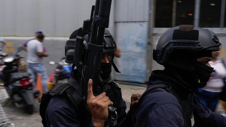 A closeup of a police officer wielding a machine gun while covered in protective gear.