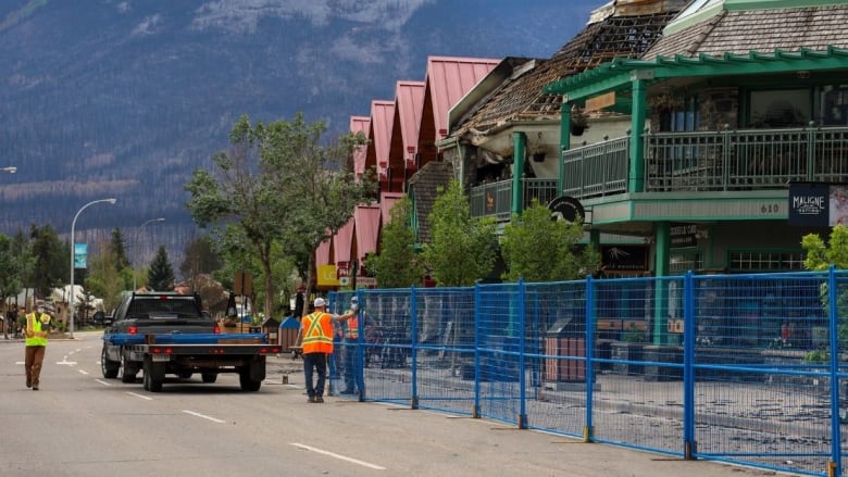 Perimeter fencing is set up around fire-damaged businesses on a street. 