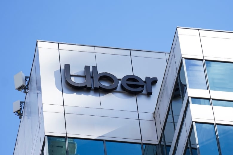 A black Uber sign on a grey building.