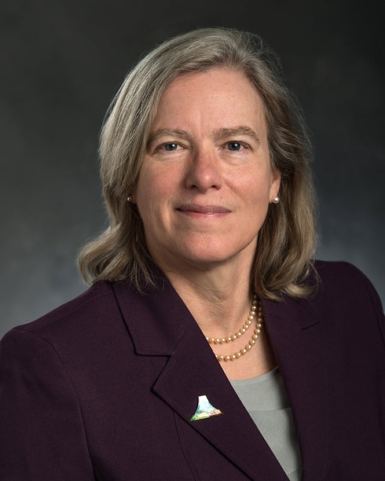 A woman with shoulder length hair wearing a burgundy jacket looks at the camera.