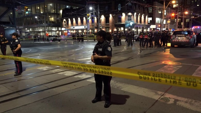 Photo showing a police officer behind yellow tape in a blocked off downtown Toronto intersection. 