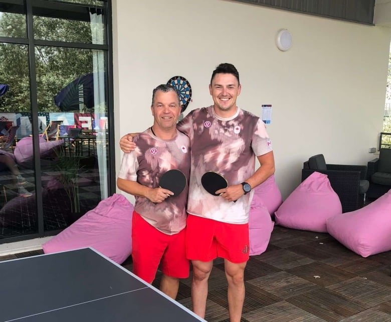 Two men holding table tennis paddles standing near a table tennis table. 