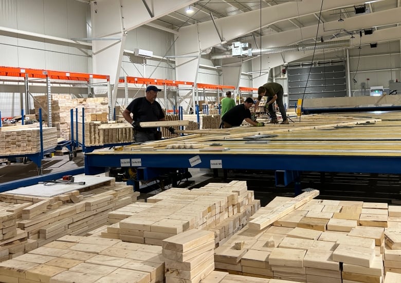 Three men working inside a lumber manufacturing business.