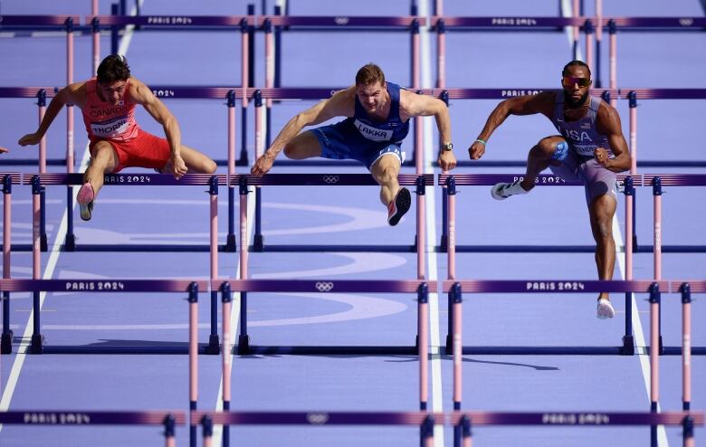 Three men hurdling on the track during a men's 110m race.