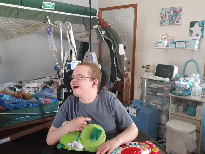 A young man in a wheelchair smiles with medical equipment behind him