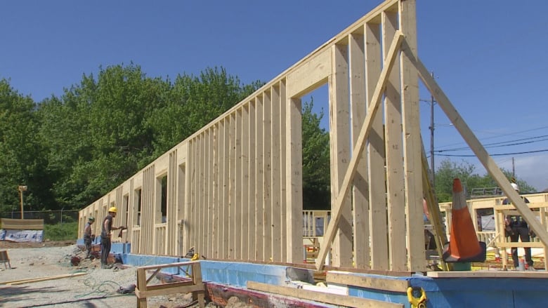 construction workers stand near a wood-framed structure of a building.