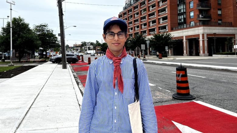 A trans person stands in front of a red bus lane. 