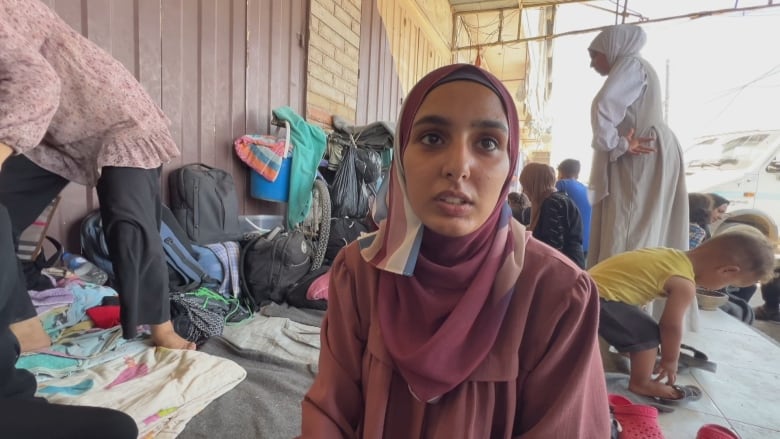 A woman in a brown dress and brown headcovering sits on the sidewalk