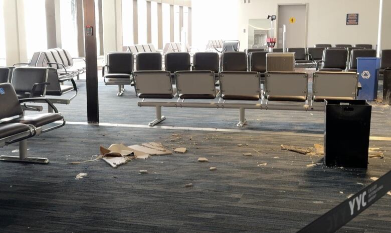 Chucks of drywall lie on the floor between waiting chairs in an airport terminal. 